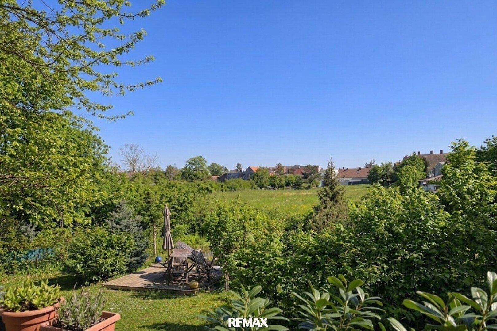 Sonnige Terrasse mit Gartenmöbeln und weitem Blick über grüne Felder.
