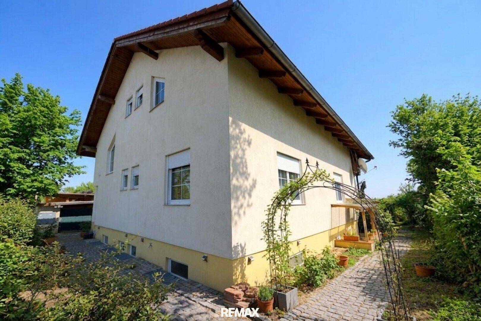 Seitenansicht des Hauses mit gepflastertem Gartenweg und üppiger Bepflanzung.