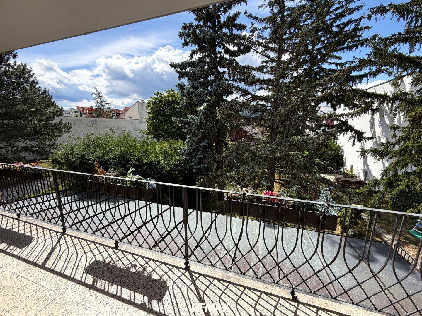 Geräumiger Balkon mit schmiedeeisernem Geländer und Blick ins Grüne.