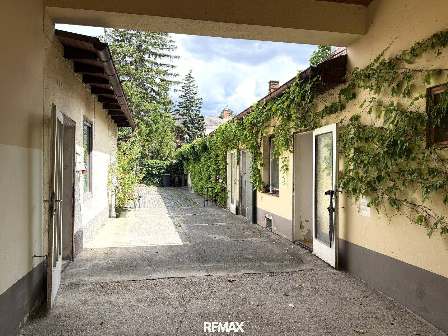 Überdachter Durchgang zu einem Innenhof mit begrünten Wänden und Nebengebäuden.