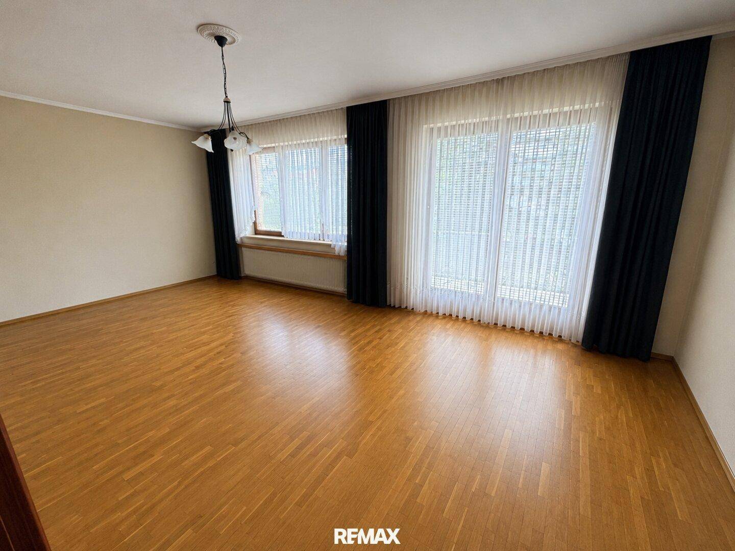Heller Raum mit Parkettboden und großen Fenstern, die viel Tageslicht hereinlassen.