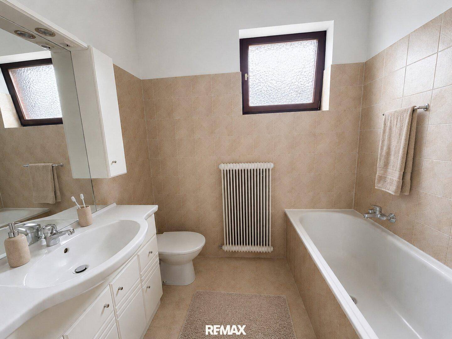 Badezimmer mit beigefarbenen Fliesen, Badewanne, Einzelwaschbecken und Fenster.