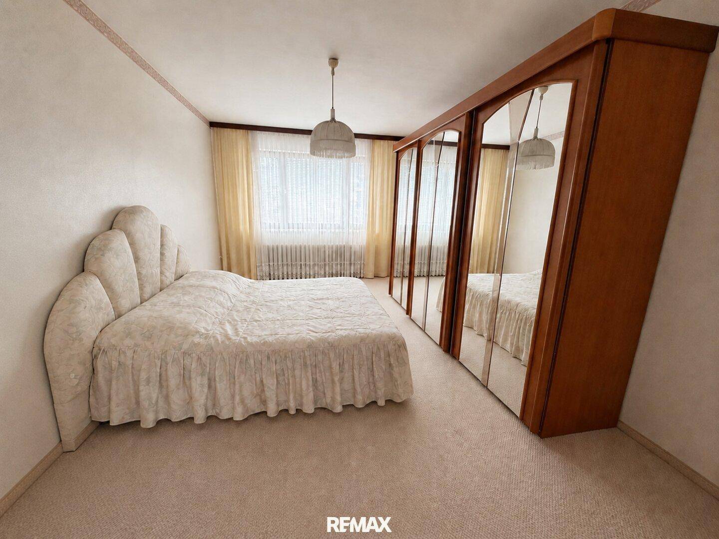 Helles Schlafzimmer mit Teppichboden, großem Spiegelschrank und gepolstertem Bett.
