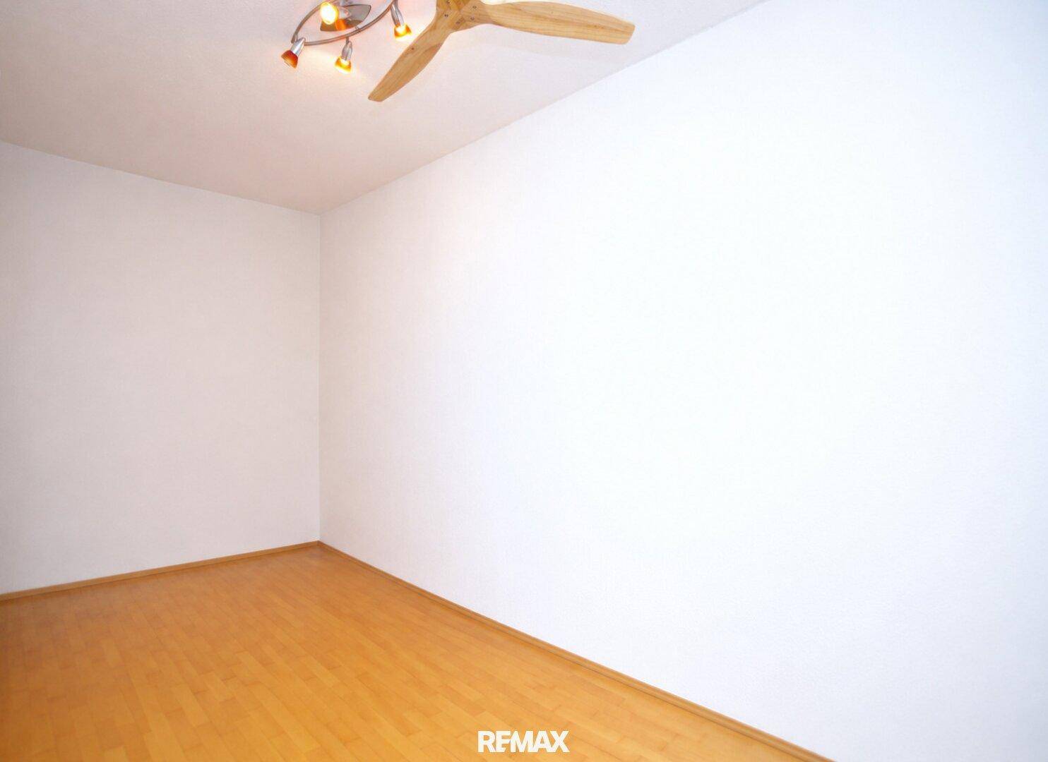 Leeres Schlafzimmer mit Holzboden, weißen Wänden und einem Deckenventilator.