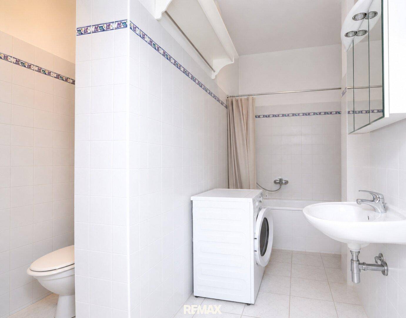 Gefliestes Badezimmer mit Badewanne, Waschbecken, Toilette und Waschmaschine.