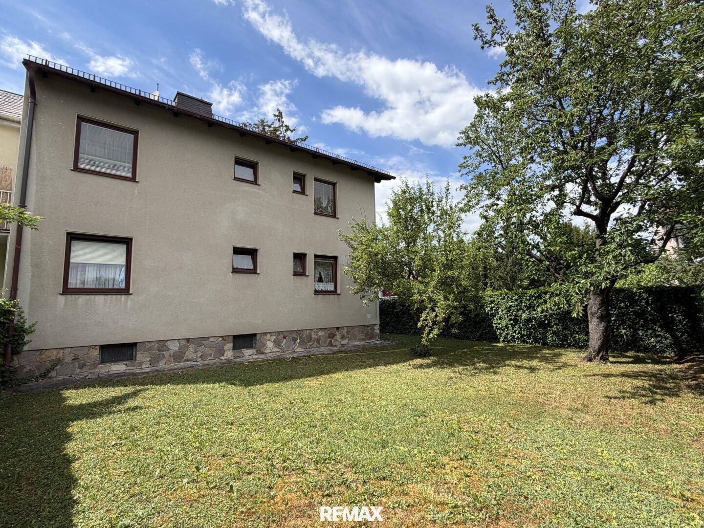 Seitliche Ansicht des Hauses mit weitläufigem Rasen und hohen Hecken im Gartenbereich.