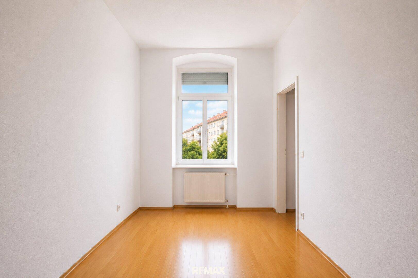 Helles, leeres Zimmer mit Holzboden, einem Fenster und Blick auf die Stadt.