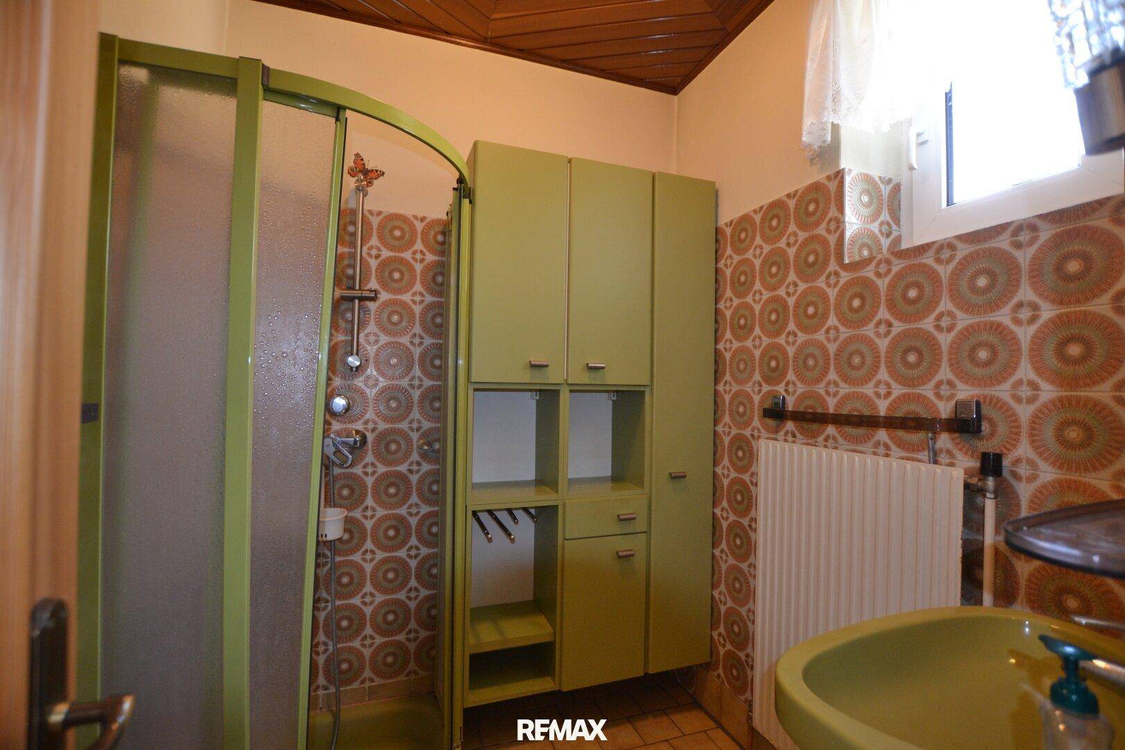 Badezimmer im Stil der 80er Jahre mit Duschkabine, grünem Waschbecken und gemusterten Fliesen.