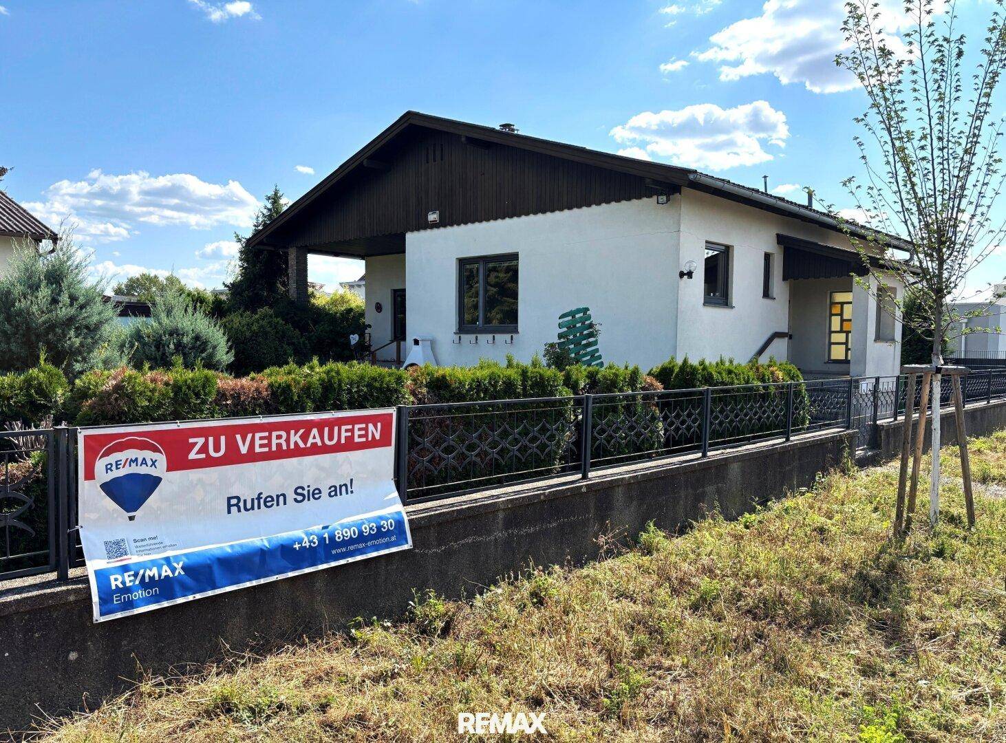 Einfamilienhaus mit "Zu Verkaufen"-Schild im Vorgarten unter blauem Himmel.