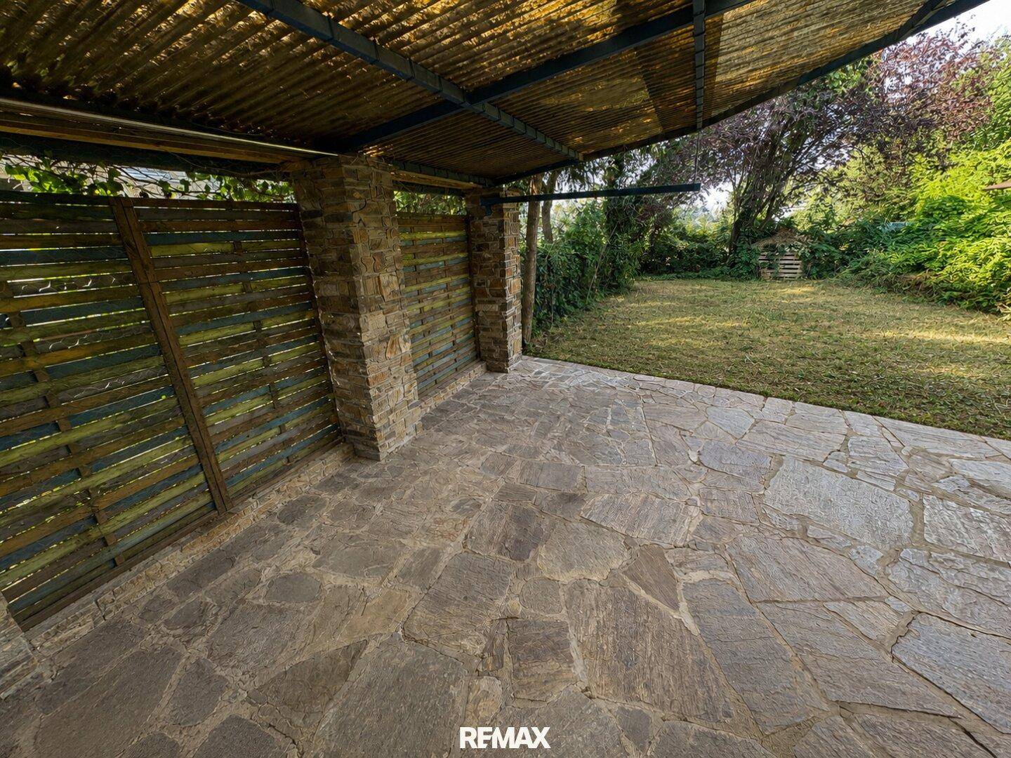 Überdachter Terrassenbereich mit Steinplattenboden und rustikalen Steinpfeilern.