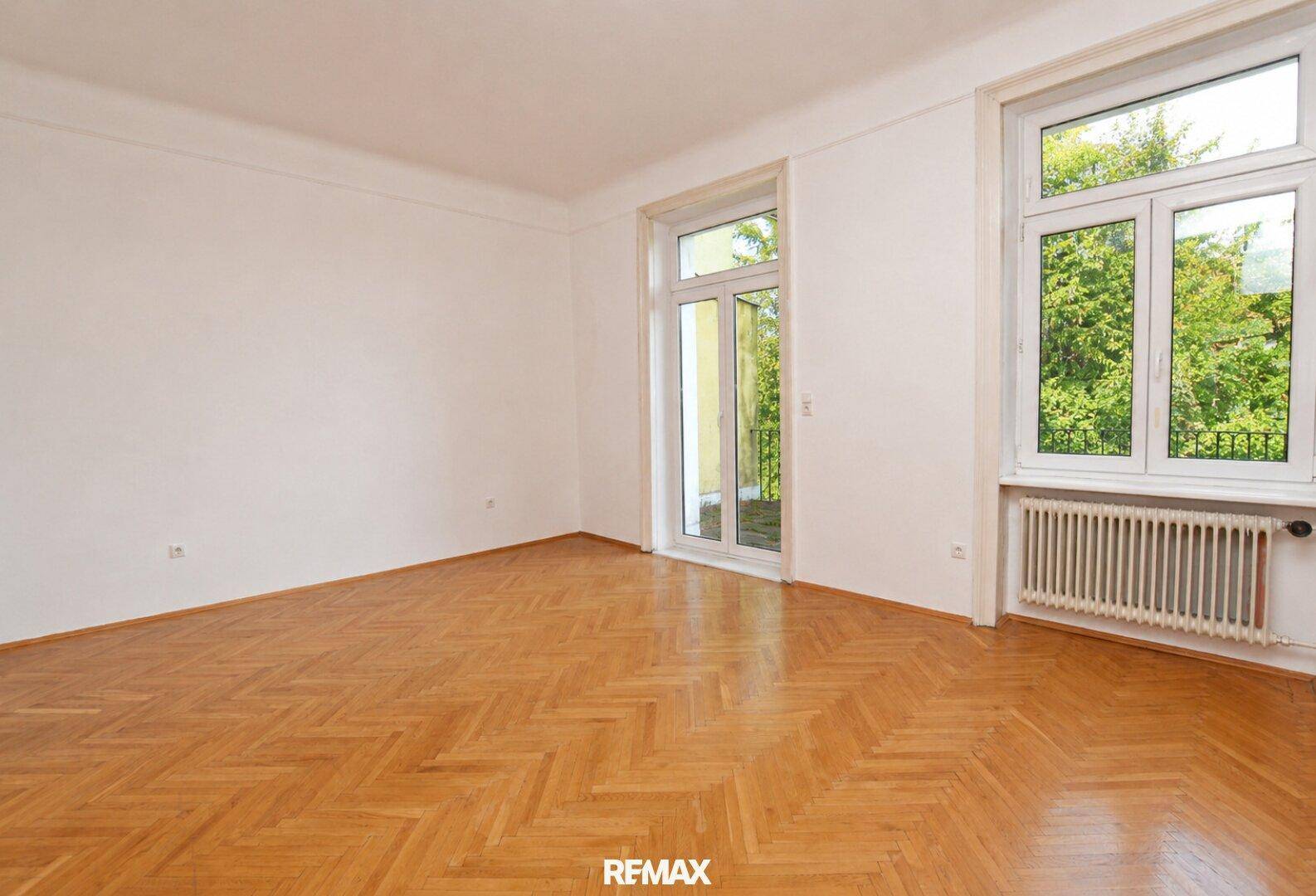 Geräumiges Zimmer mit Fischgrätparkett, großen Fenstern und direktem Balkonzugang.