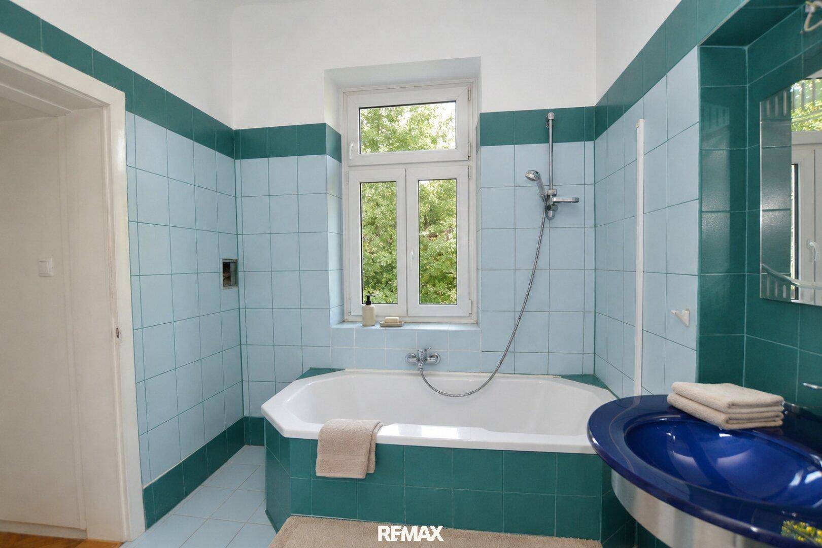 Badezimmer mit blauen Fliesen, Badewanne und Fenster für natürliches Tageslicht.