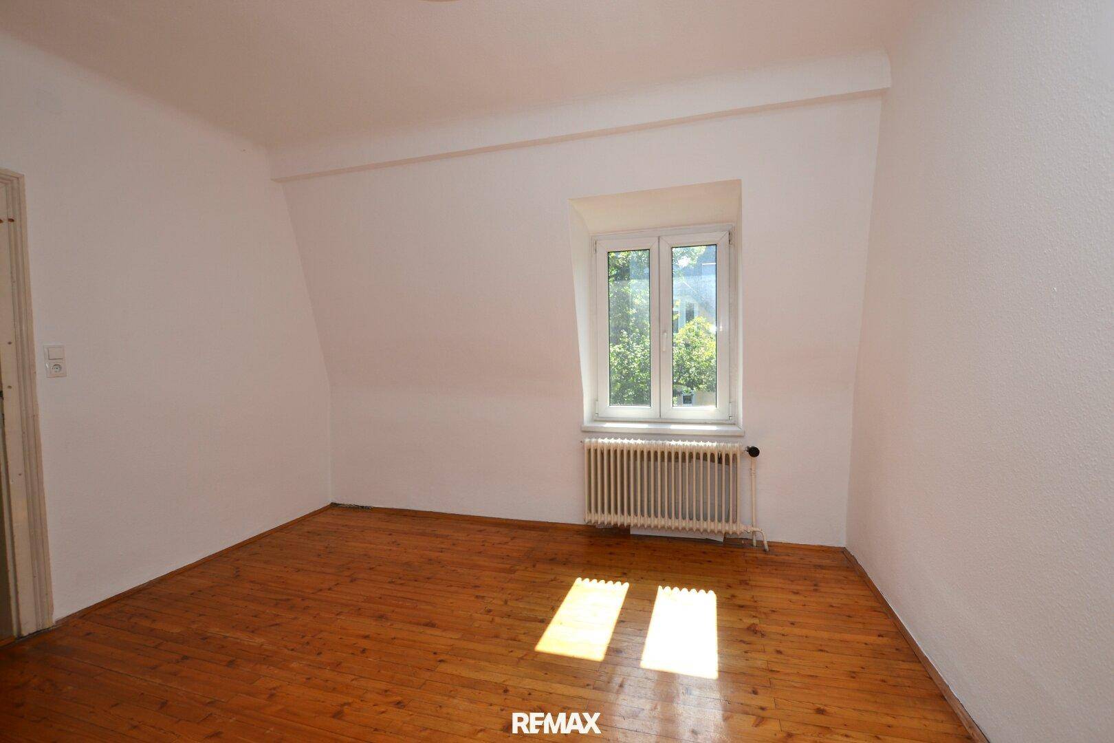 Leeres Zimmer im Dachgeschoss mit Holzdielenboden, Fenster und Heizkörper.