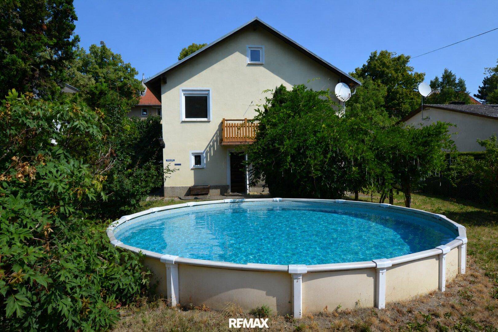 Runder Aufstellpool im Garten mit Blick auf die Hausfassade unter blauem Himmel.