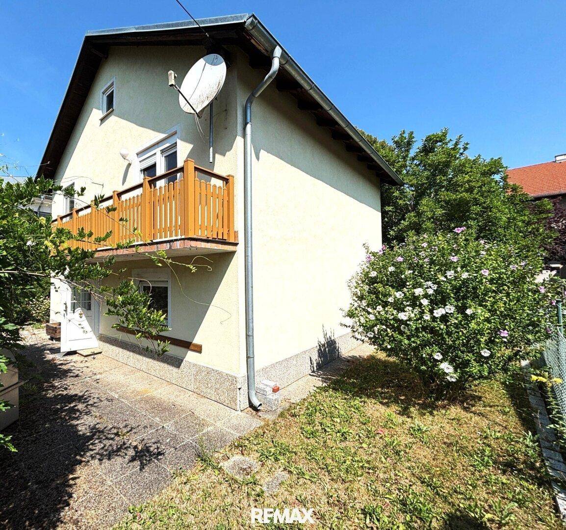 Seitenansicht des Hauses mit kleinem Holzbalkon und gepflastertem Bereich im Freien.