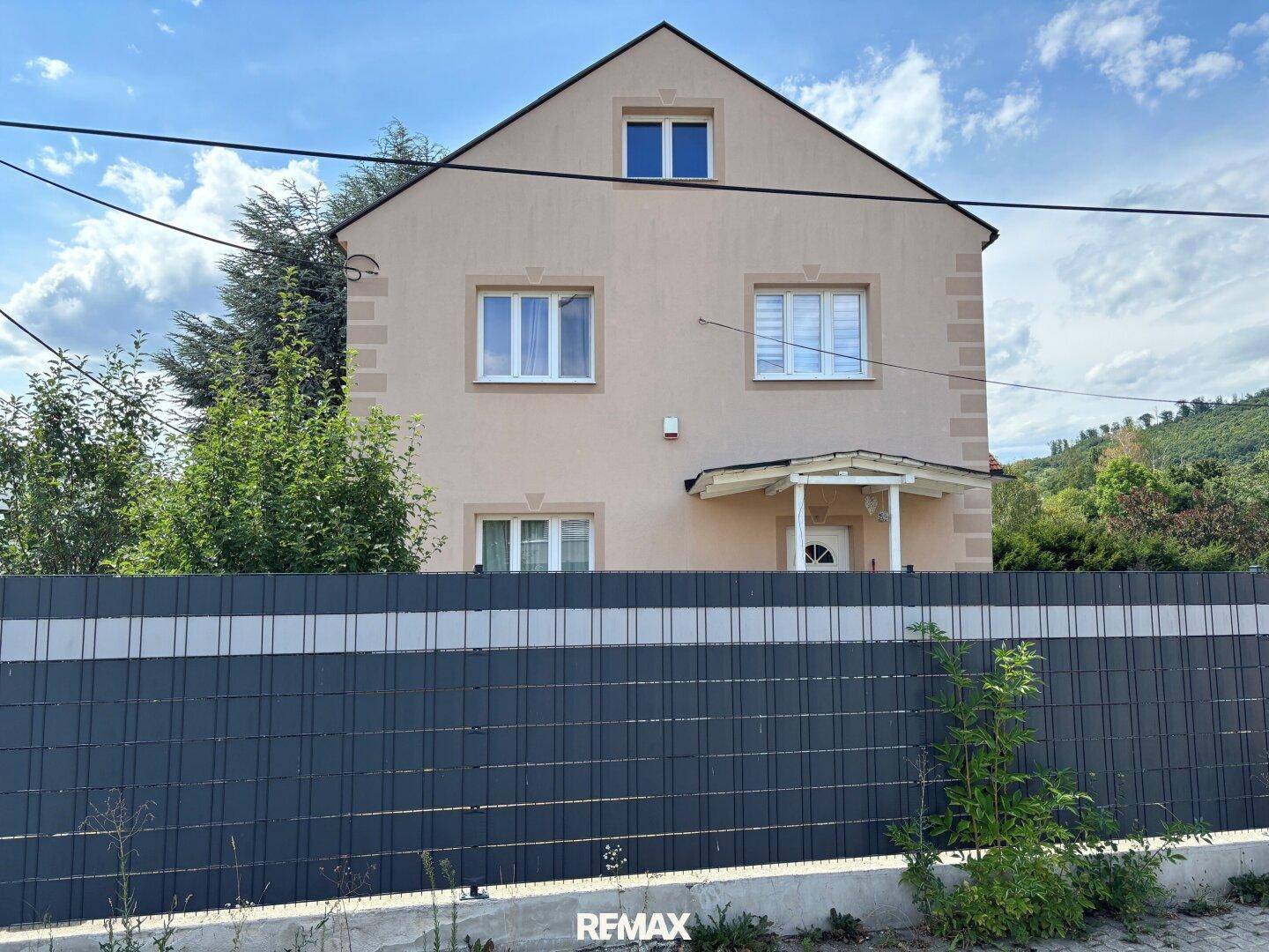 Vorderansicht des Hauses mit beiger Fassade, weißen Fenstern und einem kleinen Vordach.