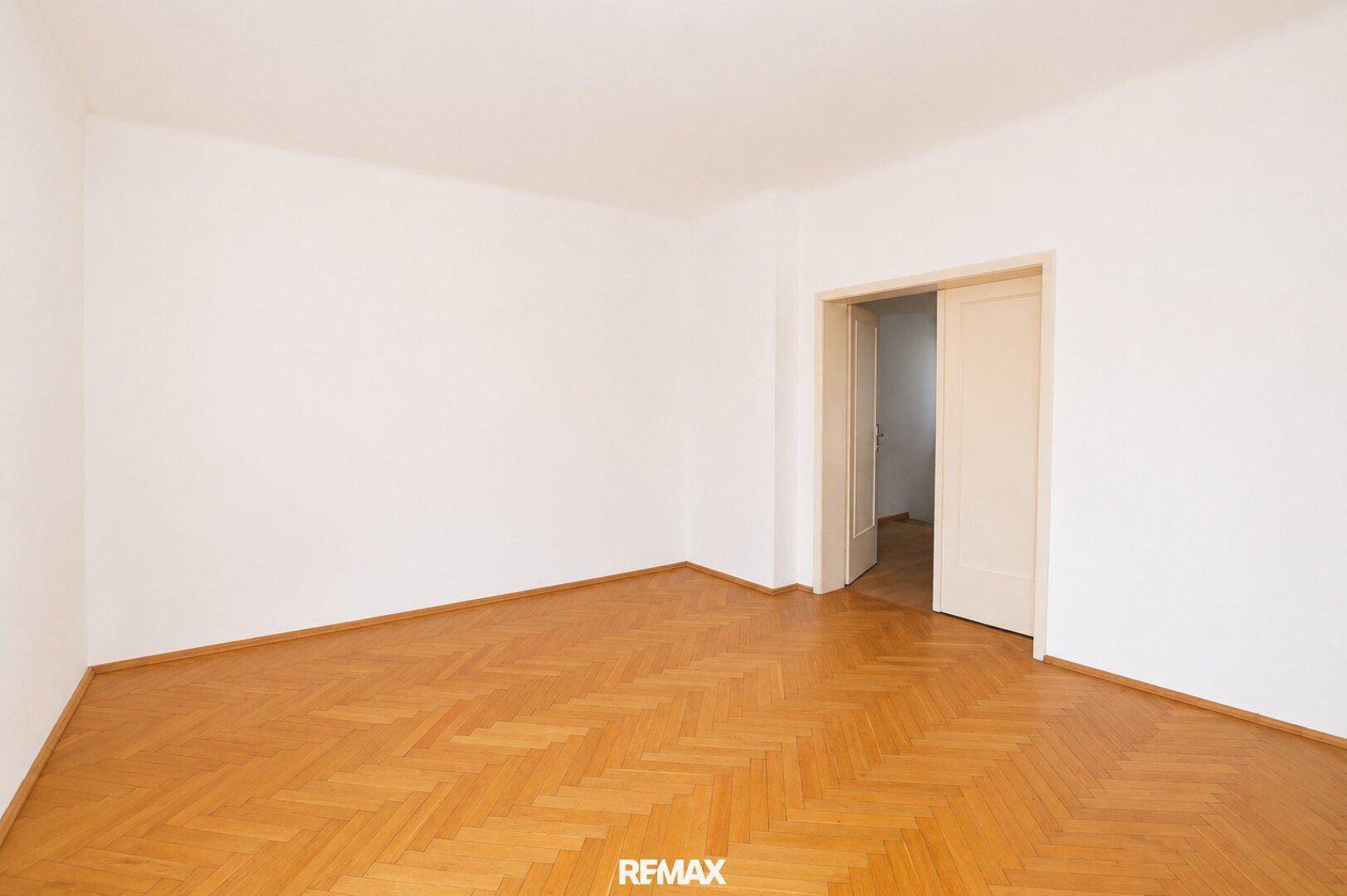 Leeres Zimmer mit Fischgrätparkett und weißen Wänden, ideal für Schlaf- oder Arbeitszimmer.