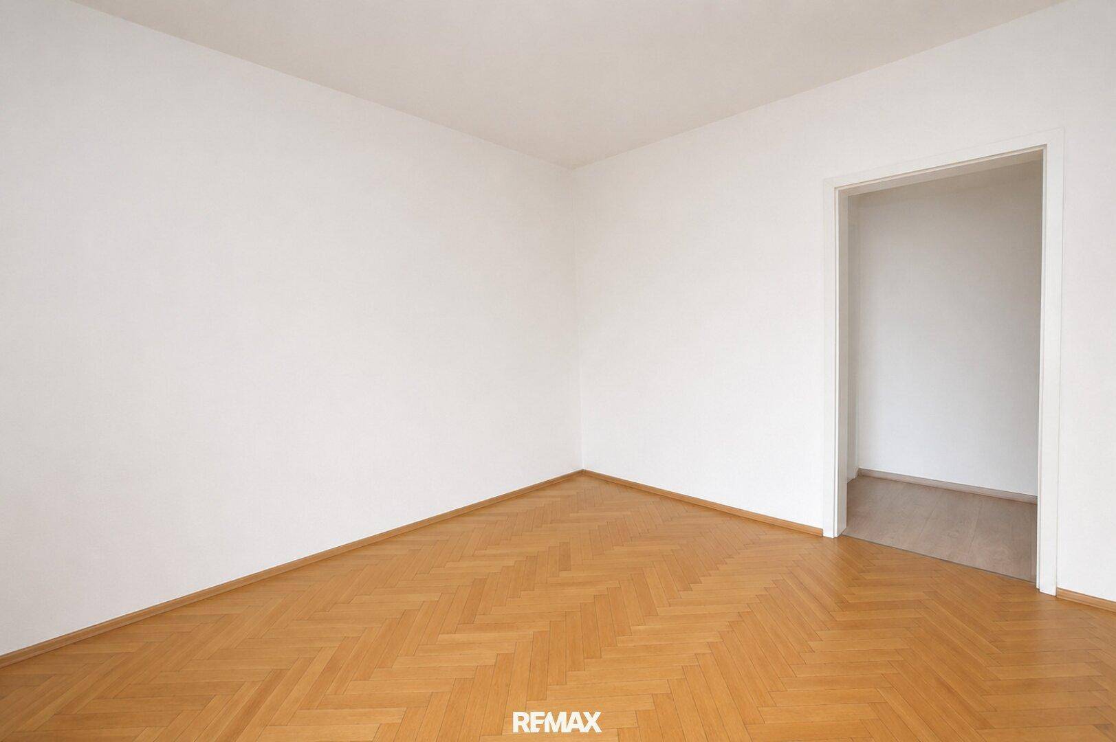Leeres Zimmer mit Fischgrätparkett und weißen Wänden, bereit zur individuellen Gestaltung.