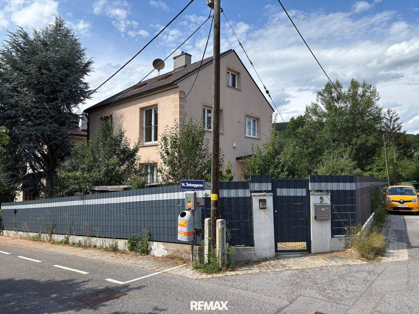 Ansicht des Hauses von der Straße mit Zaun und umliegender Vegetation.