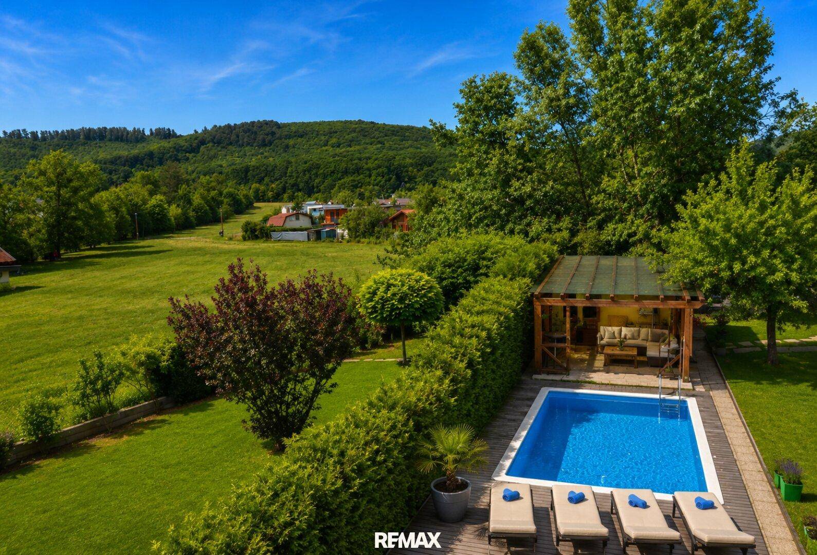 Weitläufiger Gartenbereich mit Pool, Liegestühlen und überdachtem Sitzbereich, umgeben von Natur.