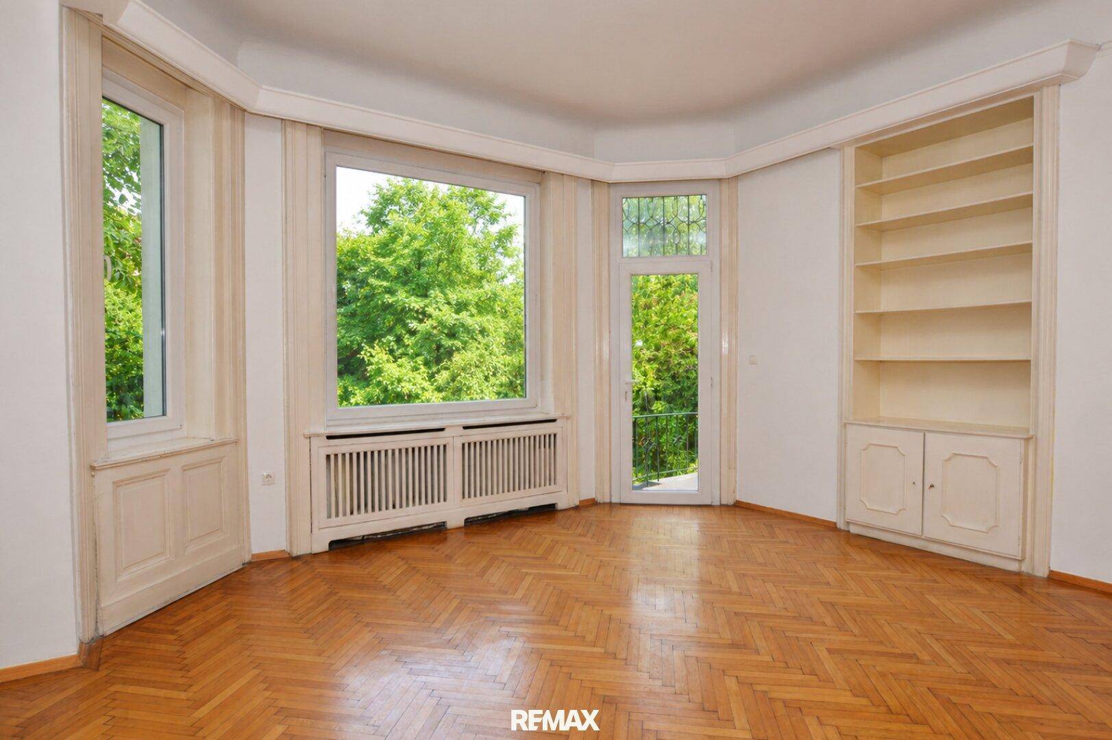 Helles Wohnzimmer mit Fischgrätparkett, großen Fenstern und eingebautem Bücherregal.