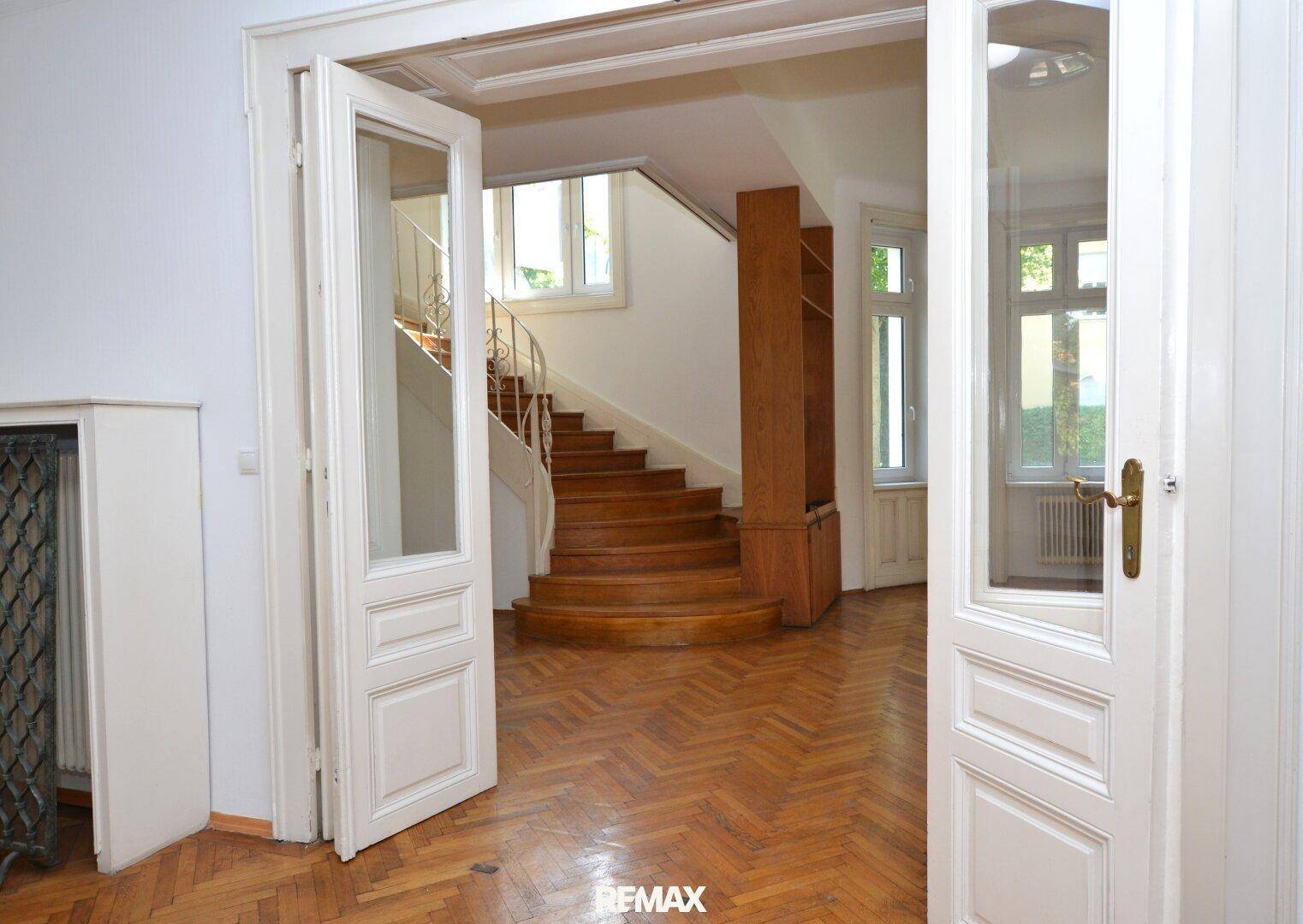Geräumiger Flur mit eleganter Holztreppe, Fischgrätparkett und hohen Doppeltüren.