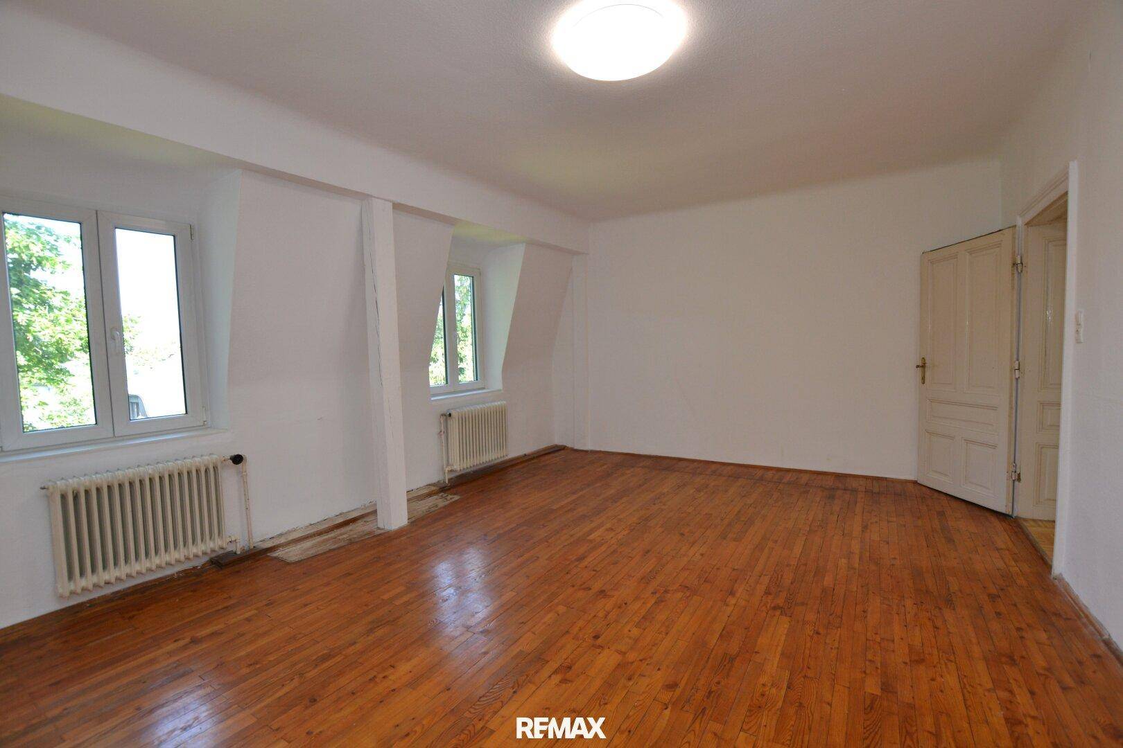 Helles Zimmer im Dachgeschoss mit Holzdielenboden, schrägen Wänden und Fenstern.