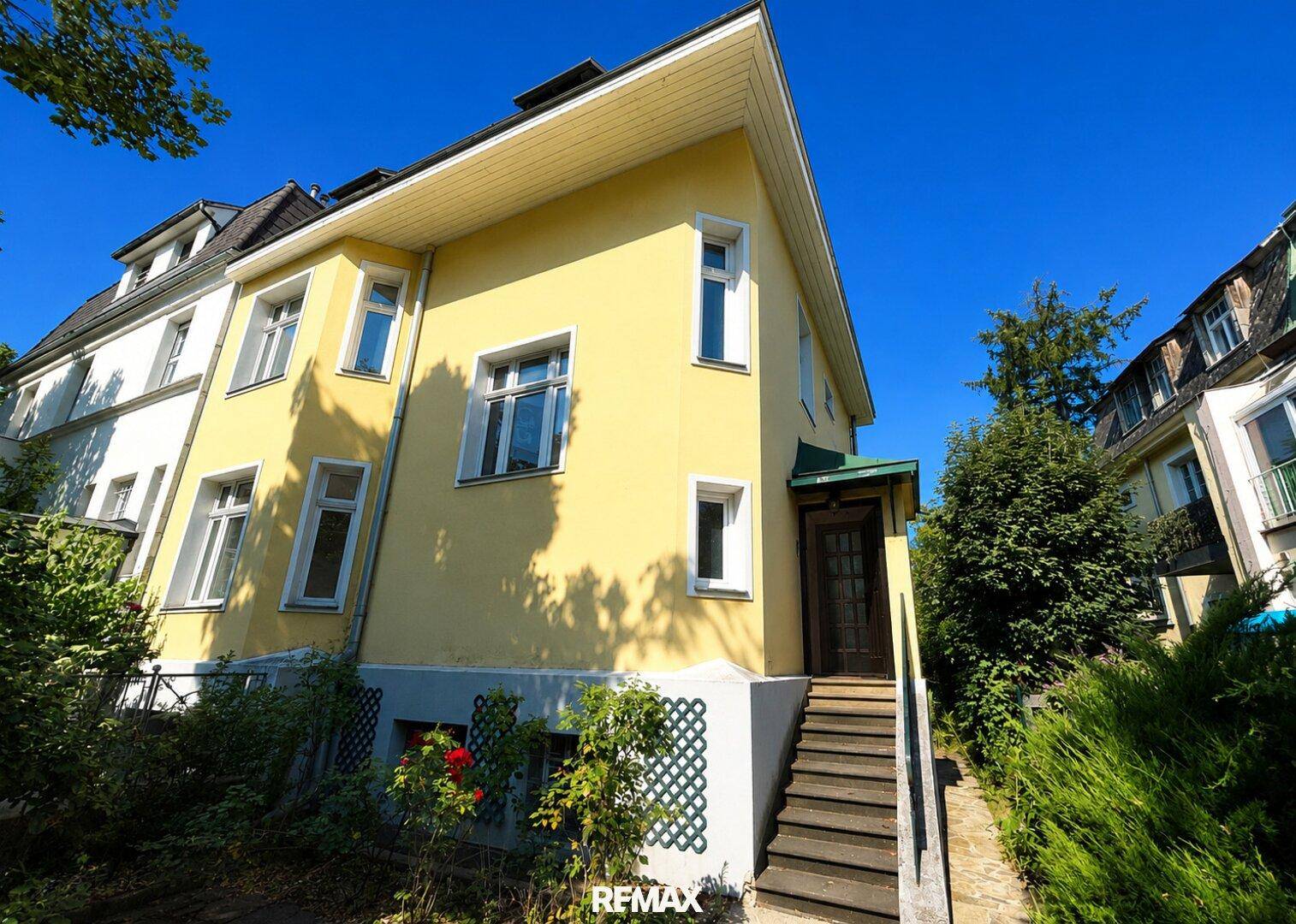 Seitenansicht der gelben Villa mit Eingangsbereich und Treppe zum unteren Gartenniveau.