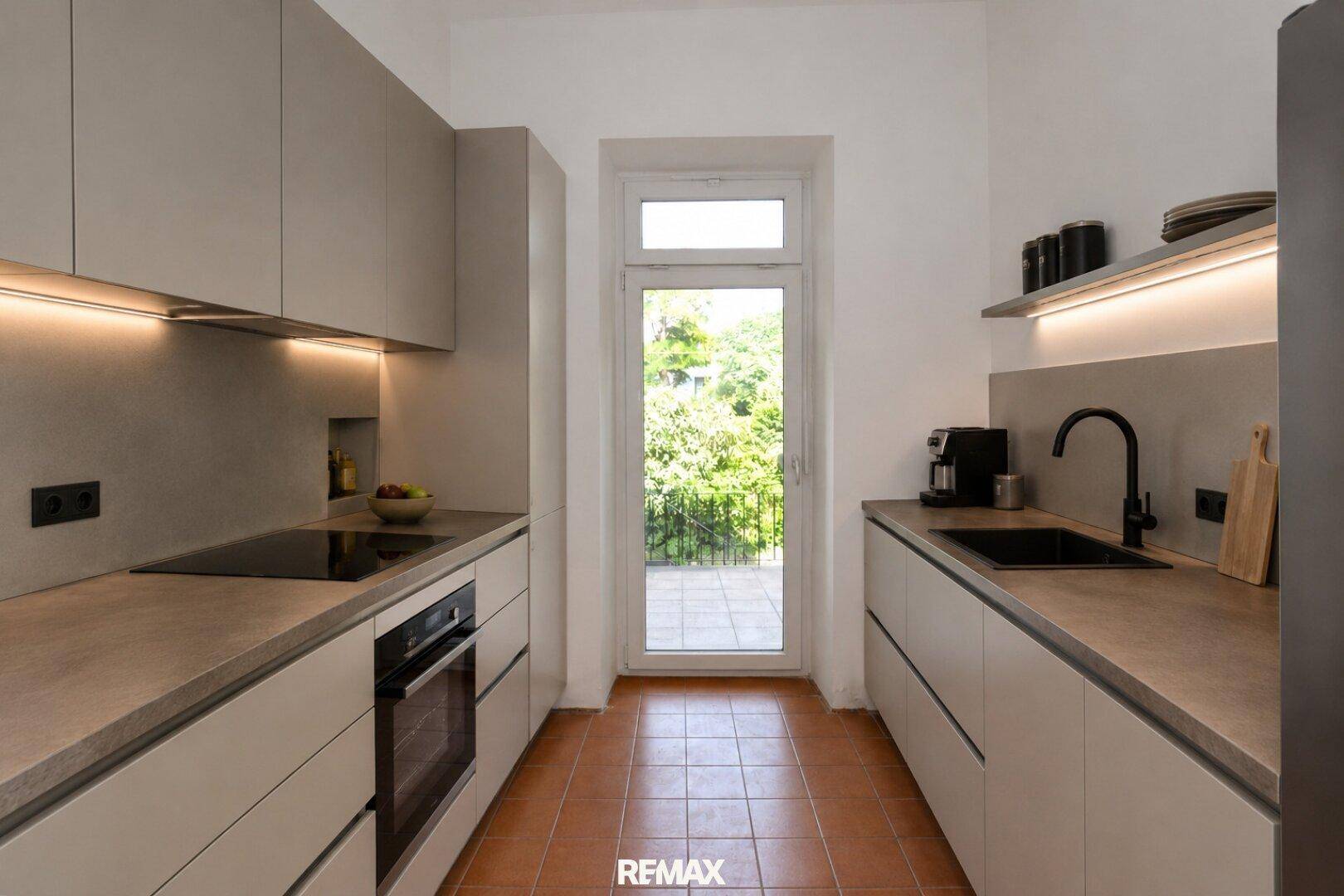 Moderne Küche mit beigen Schränken, Induktionskochfeld und Zugang zur Terrasse.