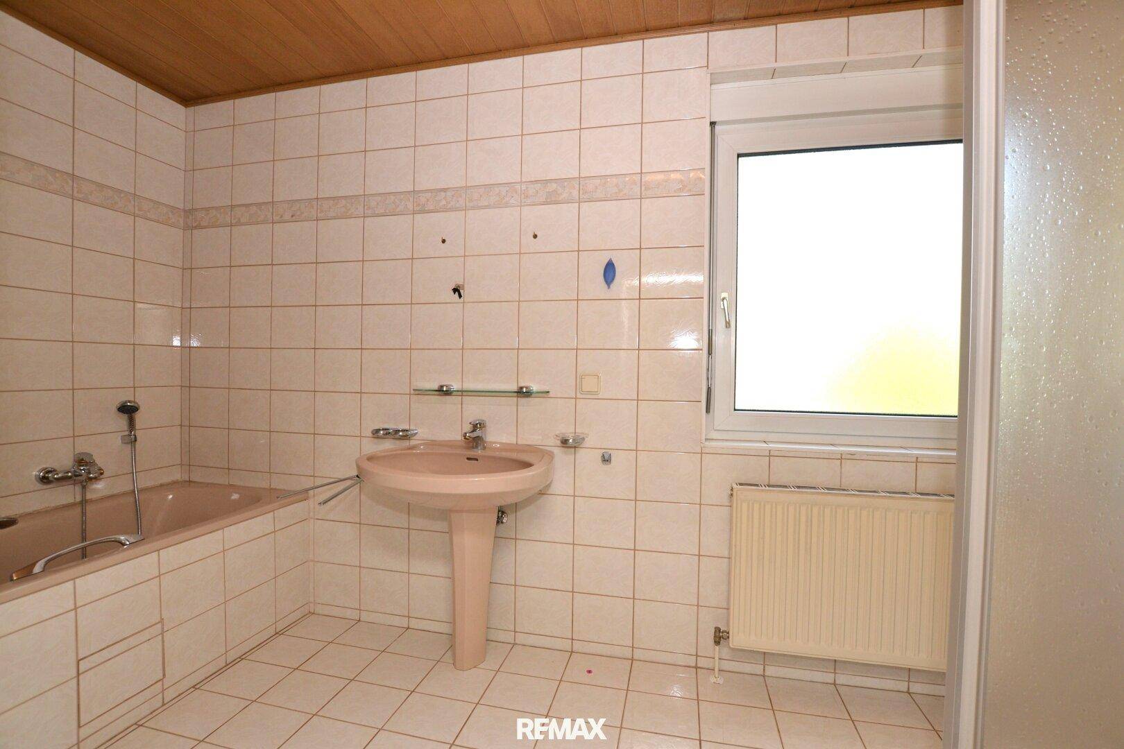 Badezimmer in ursprünglichem Zustand mit Badewanne, Fliesen und Fenster.