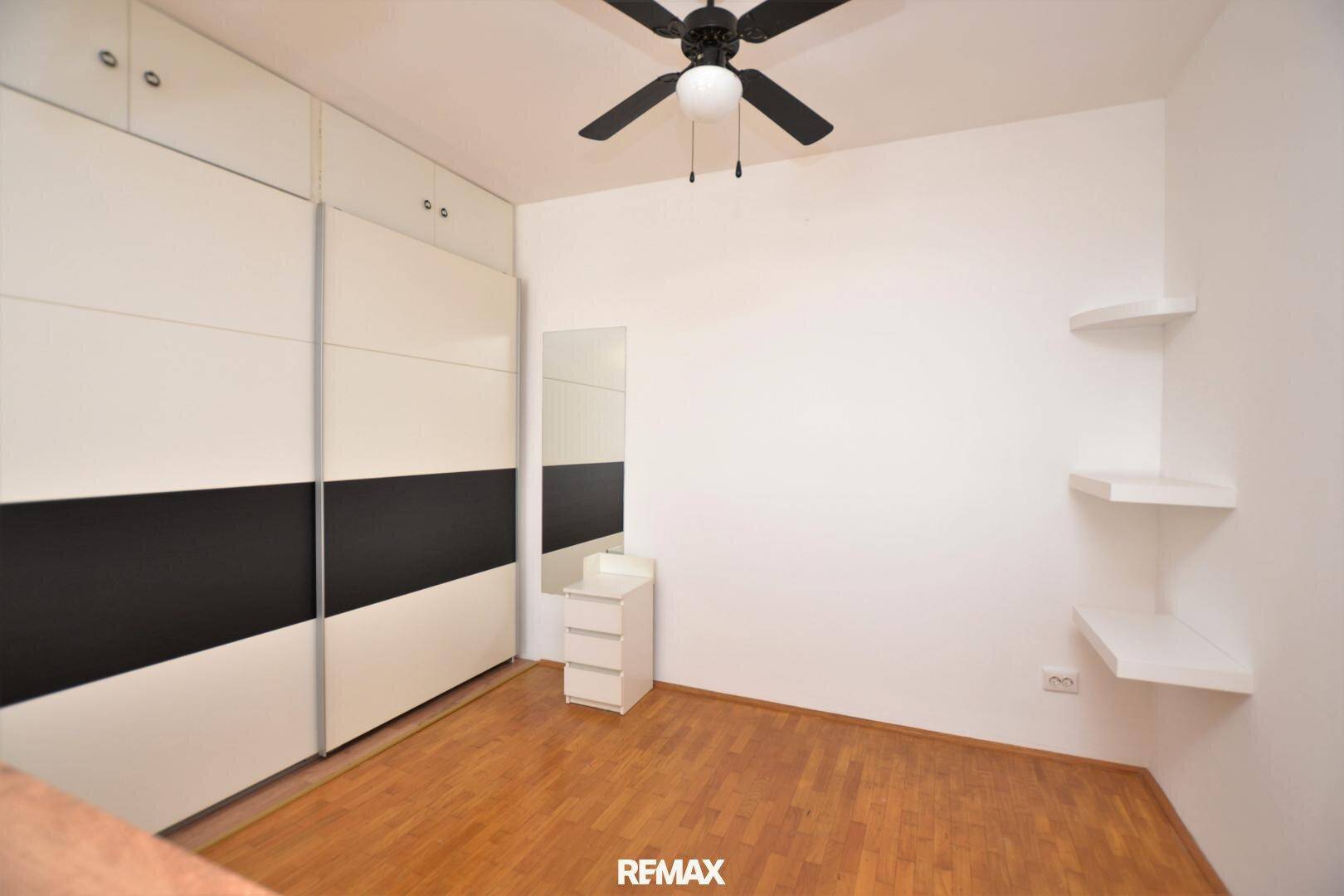 Schlafzimmer mit großem Einbauschrank, Deckenventilator und Parkettboden.