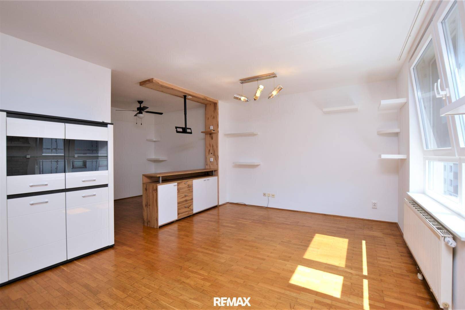 Geräumiger Wohnbereich mit Parkettboden, Deckenventilator und modernen Regalelementen.