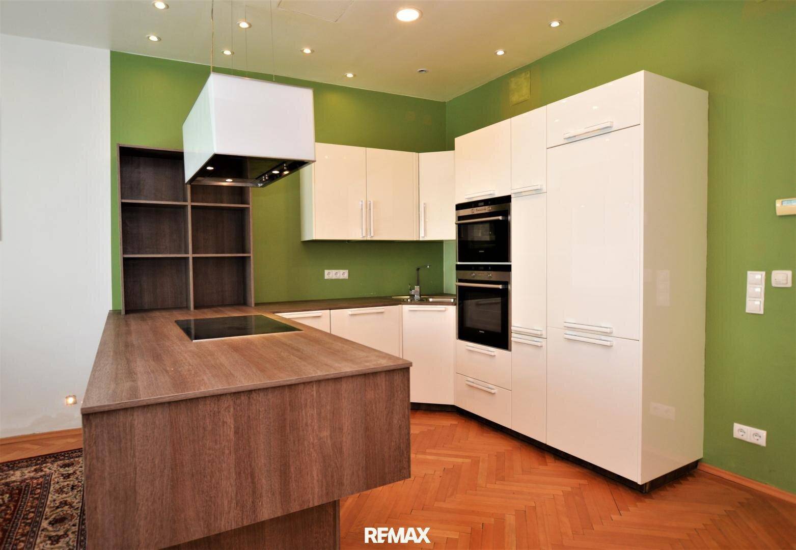 Moderne Einbauküche mit weißen Schränken, Holz-Kochinsel und integrierten Geräten in einem hellen Raum.