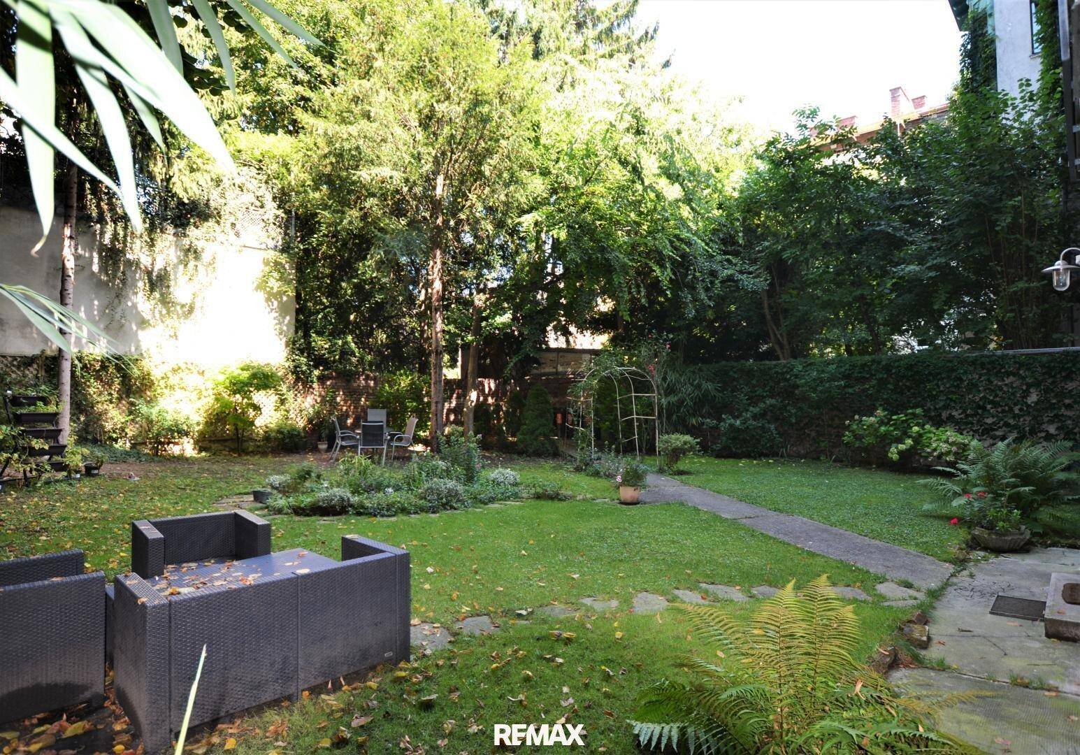 Großer, gepflegter Garten mit Rasenfläche, alten Bäumen und einer gemütlichen Sitzgelegenheit im Freien.