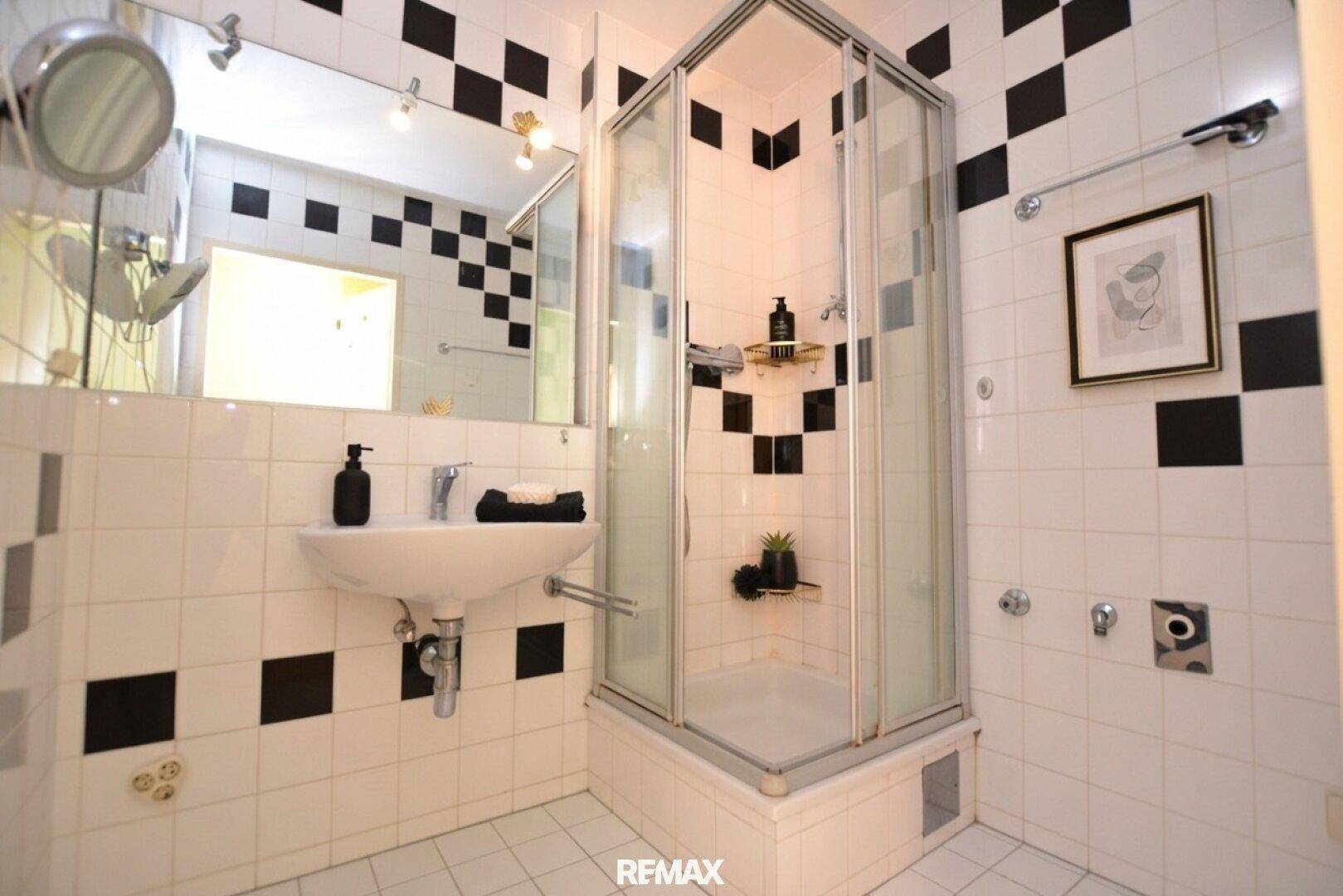 Badezimmer mit Duschkabine, Waschbecken und schwarz-weißen Fliesen.