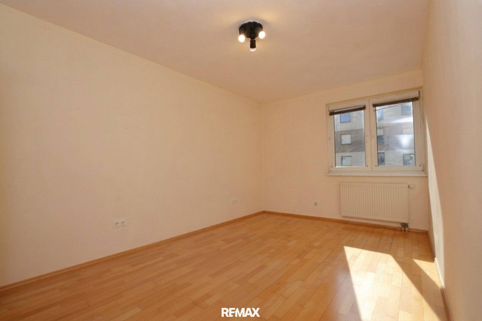 Helles Schlafzimmer mit Parkettboden und Fenster für viel Tageslicht.