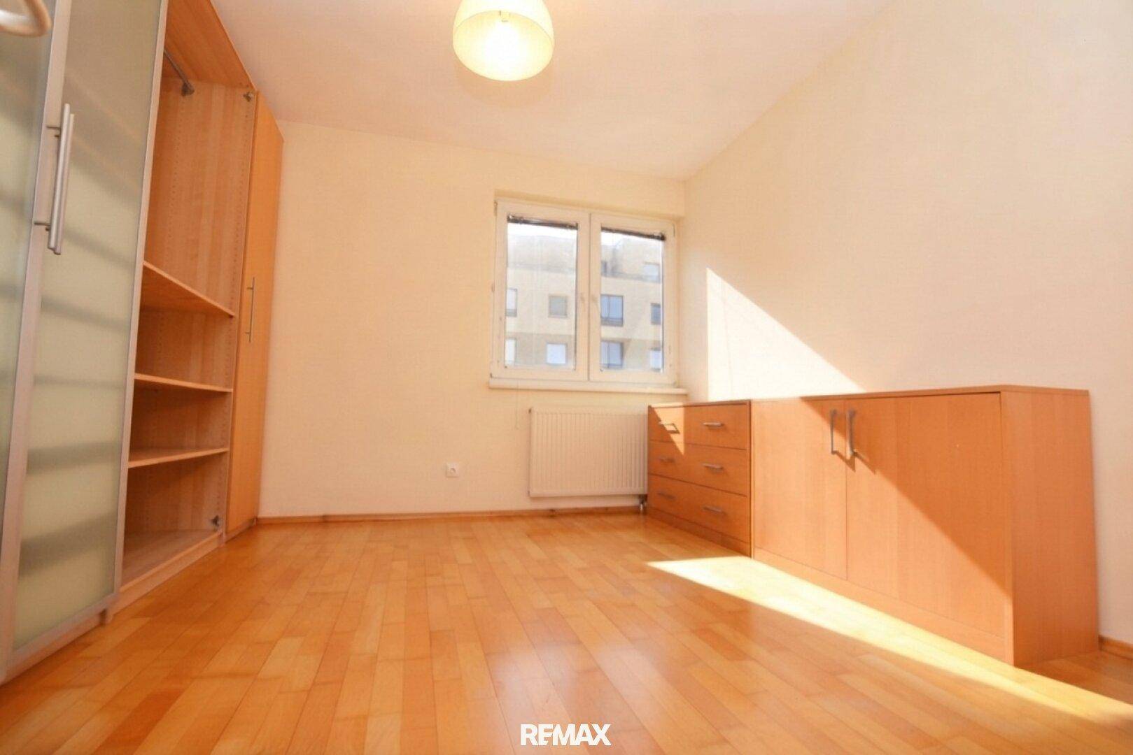 Schlafzimmer mit Parkettboden, Fenster und Einbauschrank.