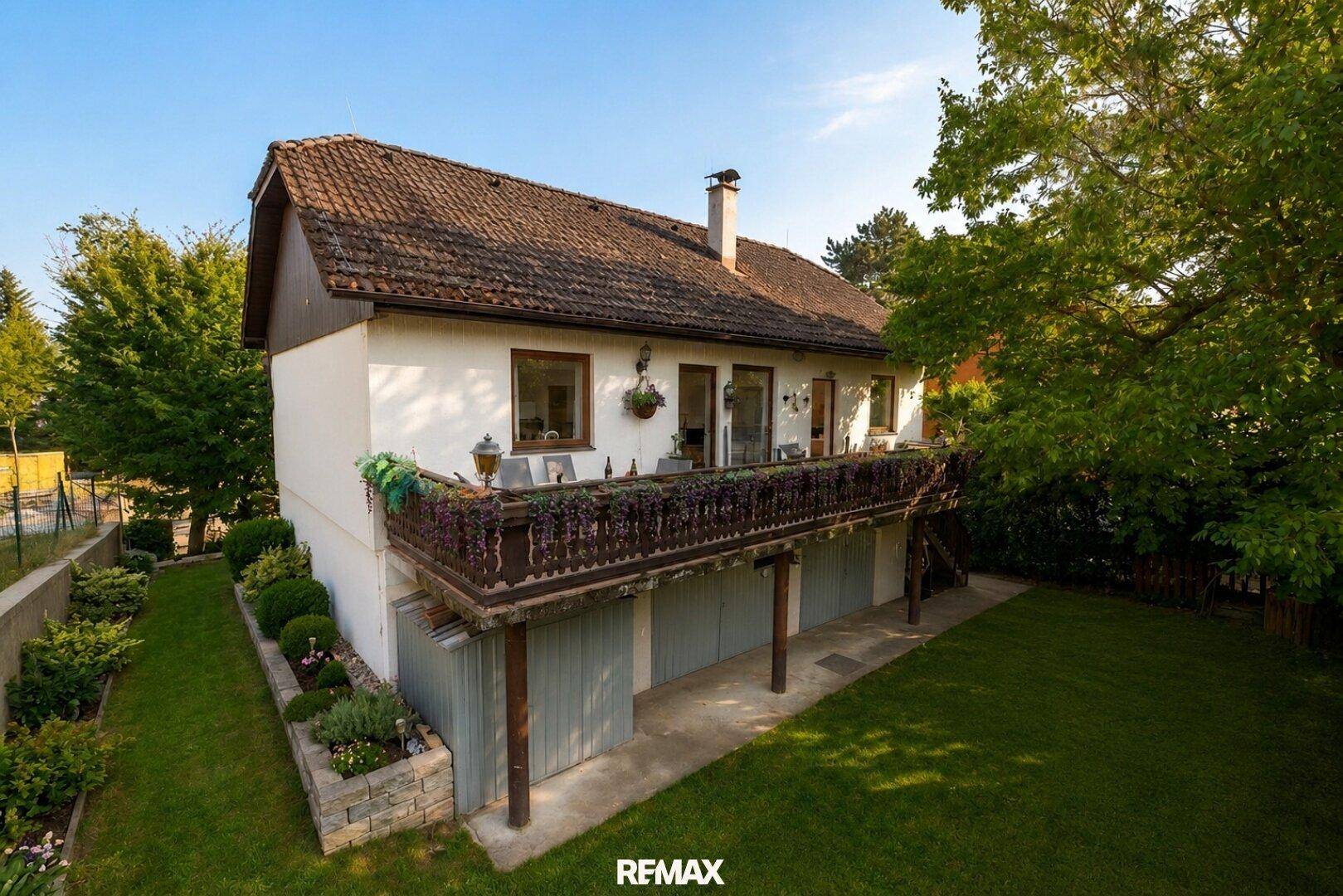 Hausfassade mit langem, traditionellem Holzbalkon und gepflegtem Gartenbereich.