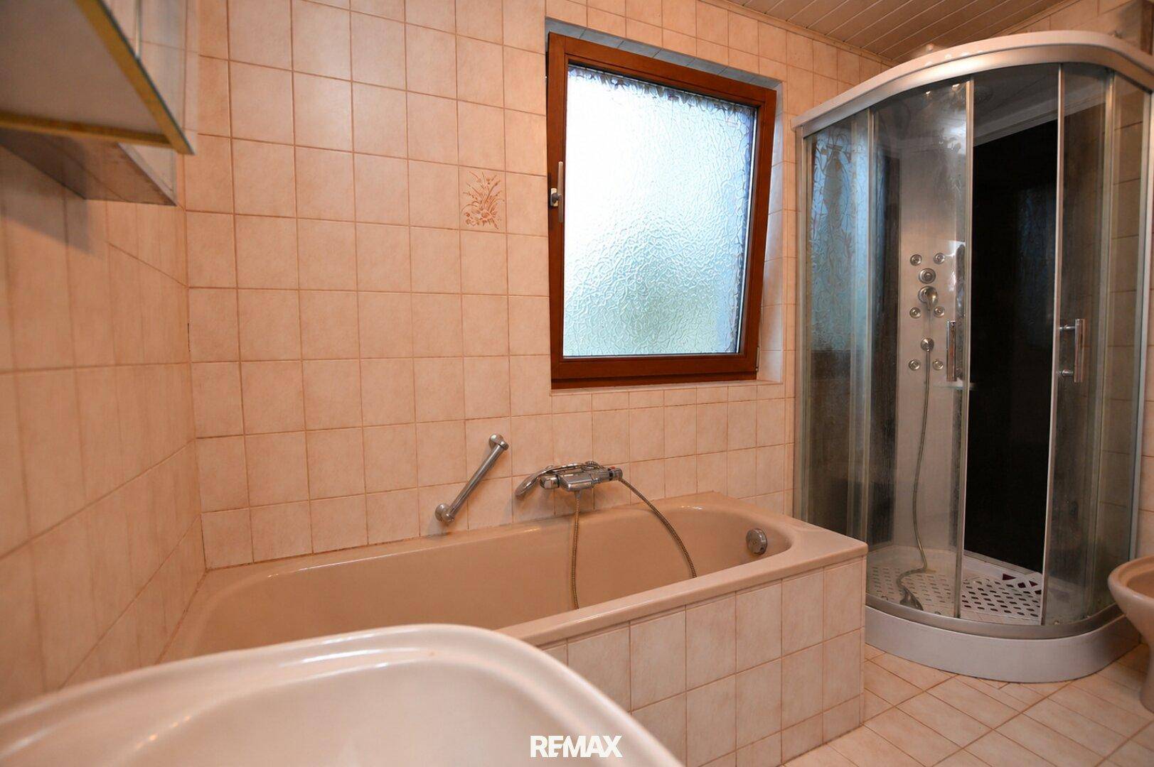 Badezimmer mit Badewanne, Duschkabine und beigefarbenen Fliesen an den Wänden.