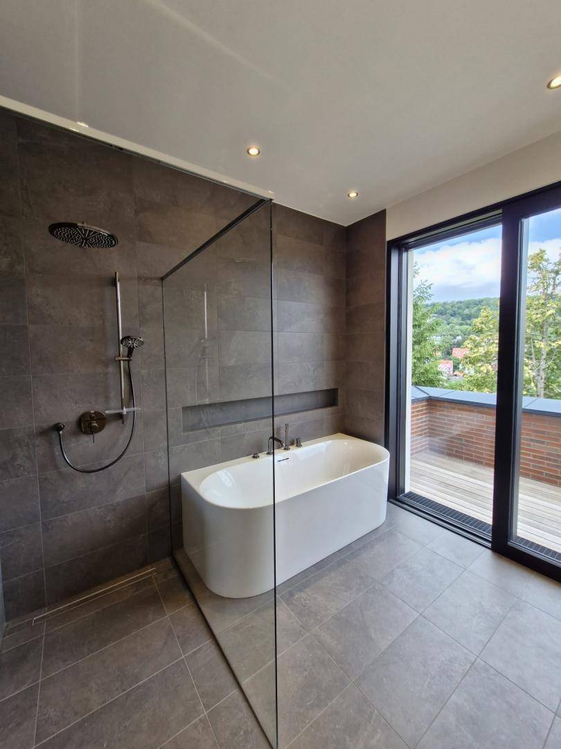 Modernes Badezimmer mit freistehender Badewanne, Regendusche und großem Fenster.