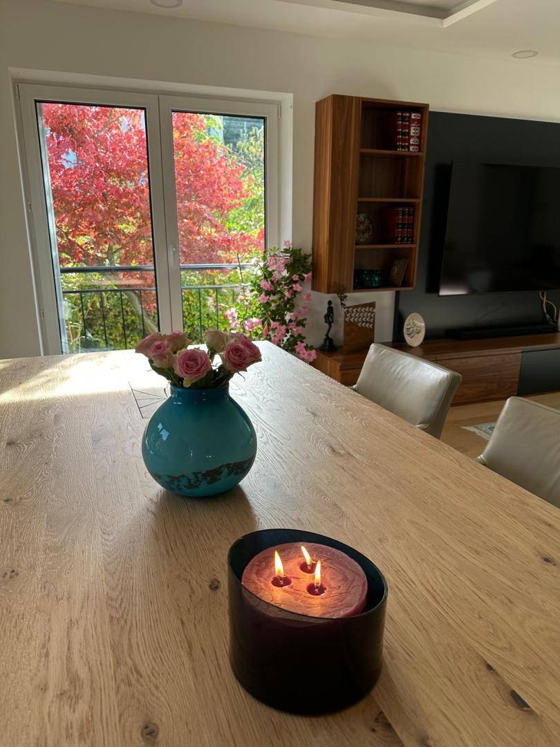 Detailaufnahme des Esstisches mit Blumenvase und Kerze, Fenster mit Herbstlaubblick.