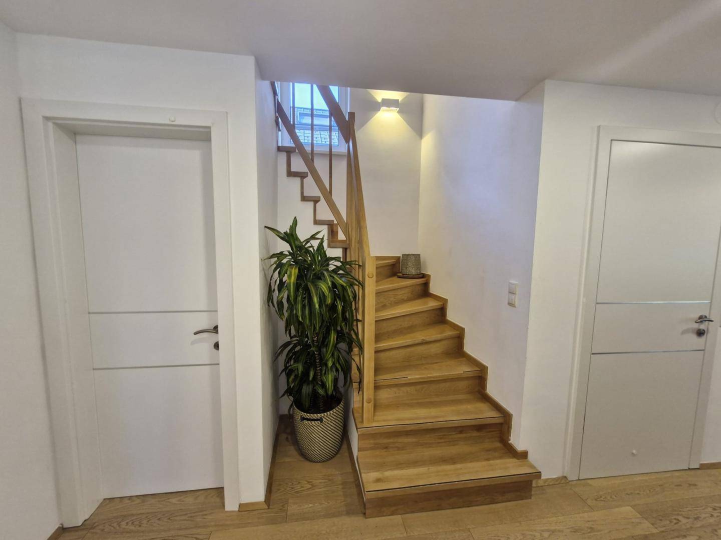 Heller Flur mit Holztreppe, weißen Türen und dekorativer Pflanze, mit Holzboden.