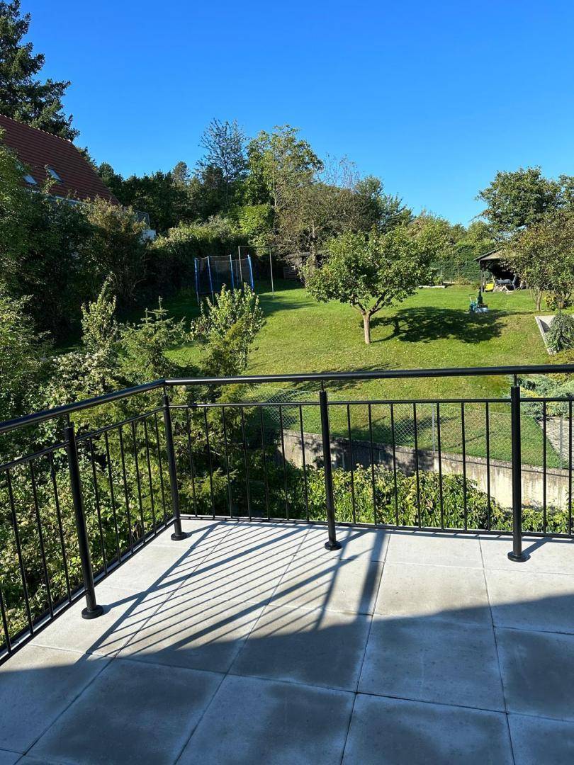 Großer Balkon mit Fliesenboden und weitem Blick auf den grünen Garten an einem sonnigen Tag.