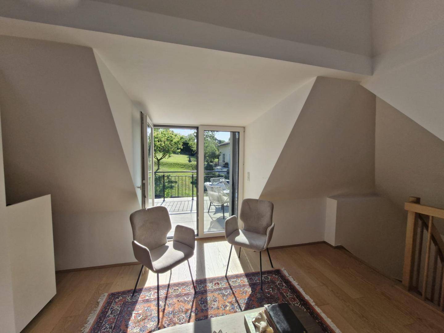 Dachgeschosszimmer mit schrägen Wänden, Holzboden und Zugang zu einem sonnigen Balkon.