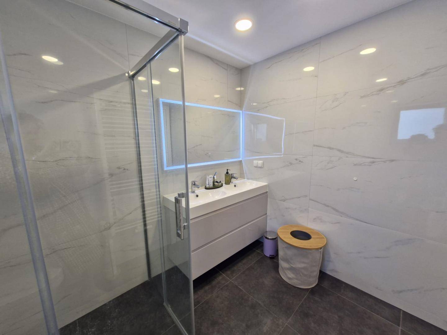 Elegantes Badezimmer mit großer Dusche, modernem Waschtisch und beleuchtetem Spiegel, mit Fliesenboden.