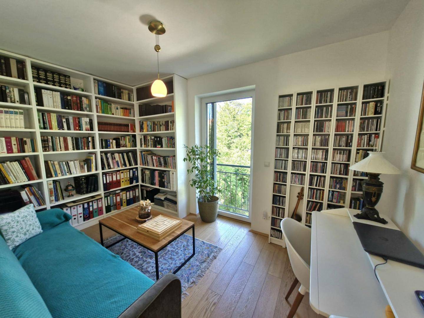 Helles Arbeitszimmer mit großen Bücherregalen, Schreibtisch und Zugang zum Balkon mit Grünblick.