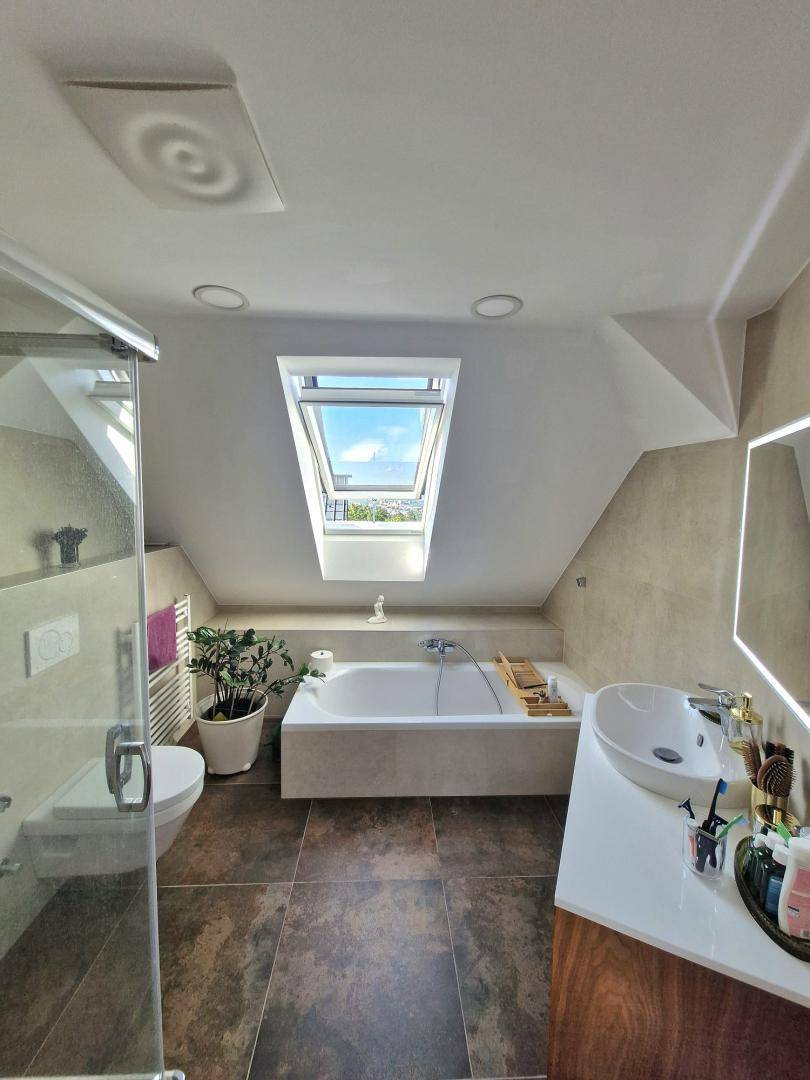 Helles Badezimmer im Dachgeschoss mit Badewanne, Waschtisch, Dusche und Dachfenster für viel Licht.