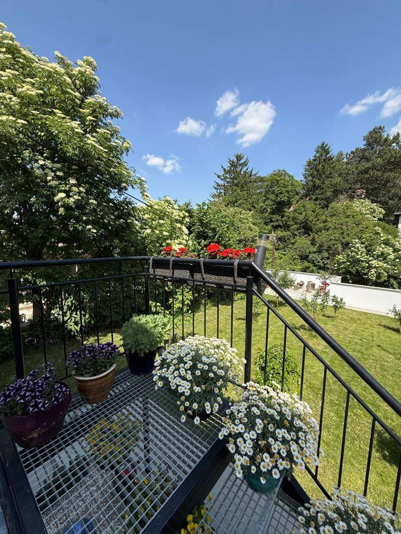 Balkon mit Treppe zum Garten, geschmückt mit bunten Blumen und Pflanzen, an einem sonnigen Tag.
