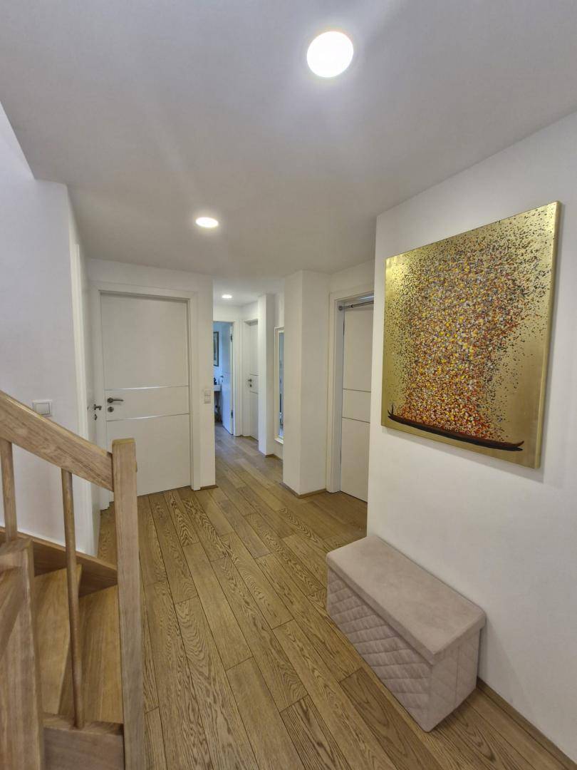 Geräumiger Flur mit Holzboden, weißer Wandgestaltung und moderner Kunst, hell beleuchtet.