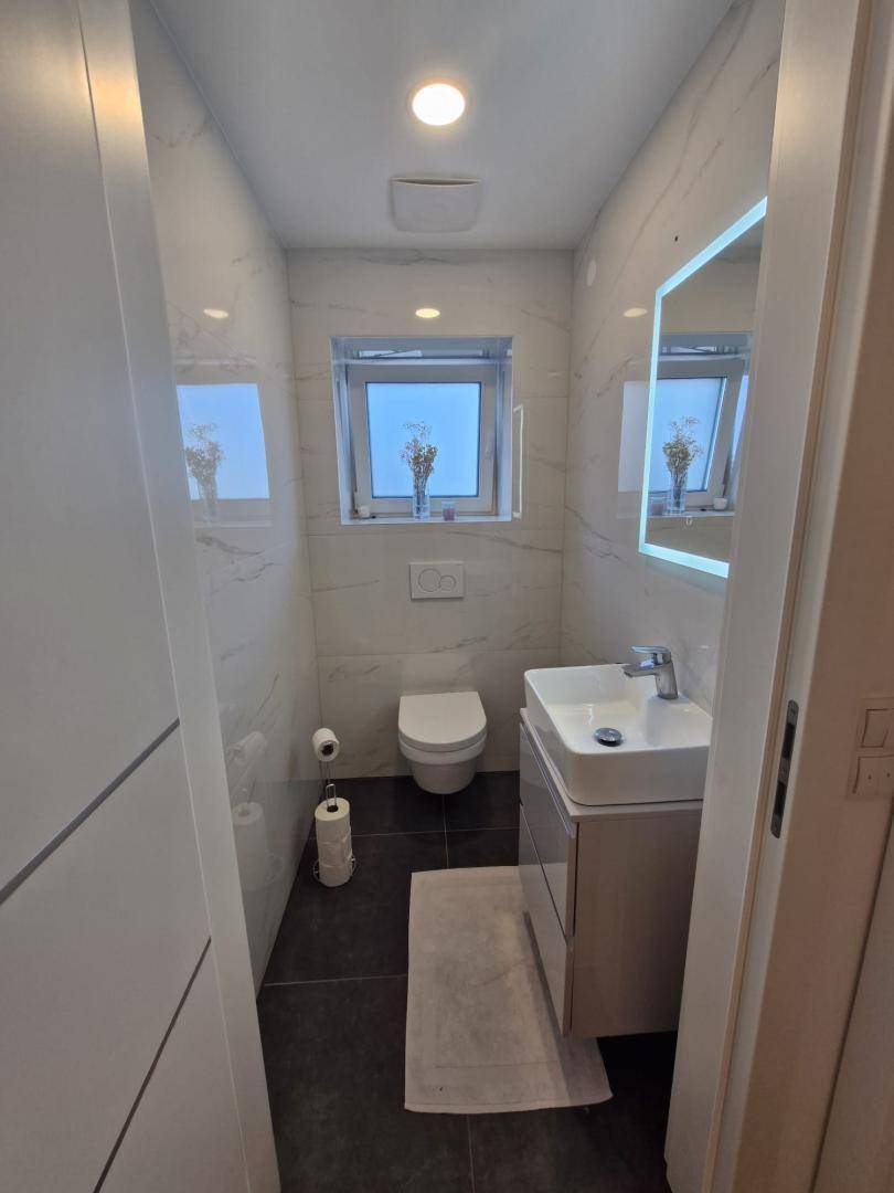 Modernes Gäste-WC mit Fenster, wandhängendem WC und kleinem Waschtisch, hell und funktional.